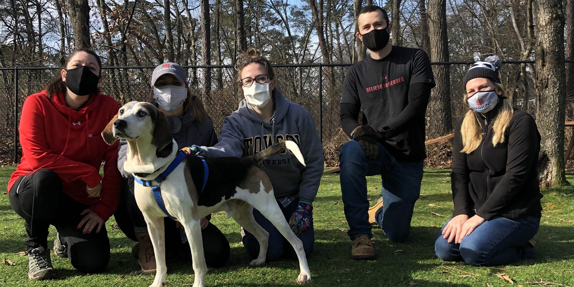 Harkins employees kneeling down in front on a turf field behind a dog.